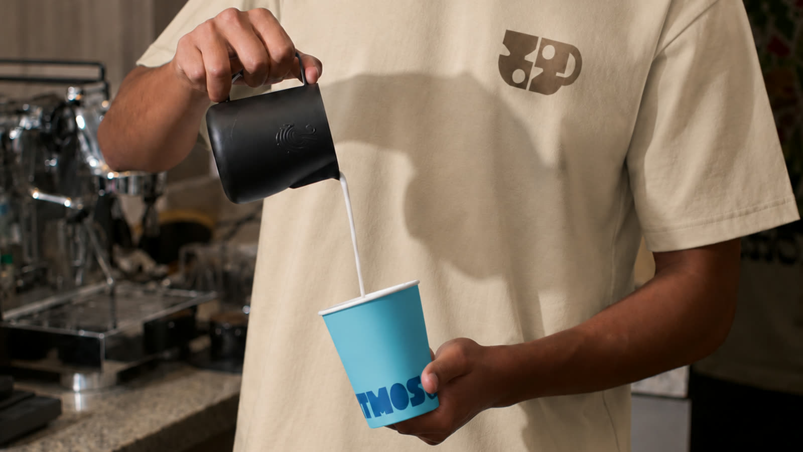 Barista Atmos turnând lapte într-un pahar albastru