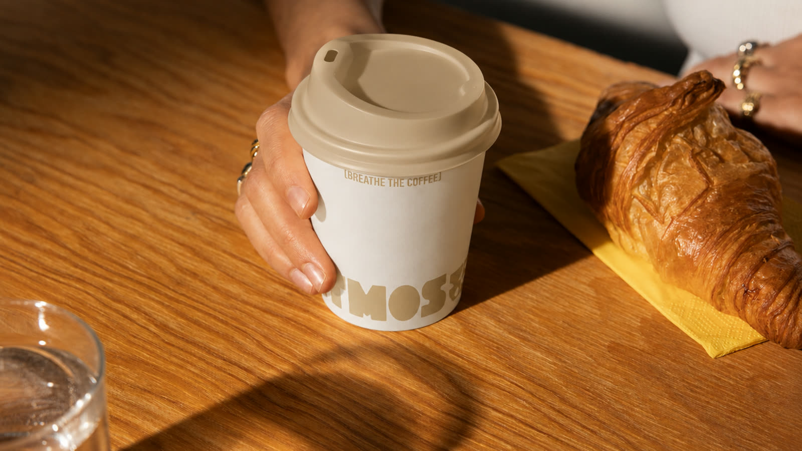 Pahar Atmos ținut în mână, lângă un croissant